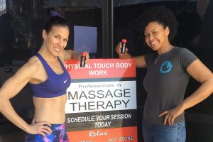 Two women holding HOTSHOT in front of Massage Therapy sign