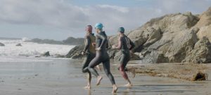 three athletes running into ocean with wetsuits